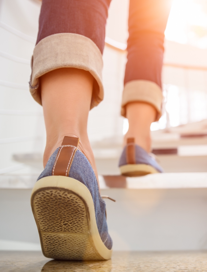 A photo showing the back of a woman's legs and feet as she walks up some stairs. Balance and Babysteps Nutrition is owned and operated by Registered Holistic Nutritionist, Shanon Menard.